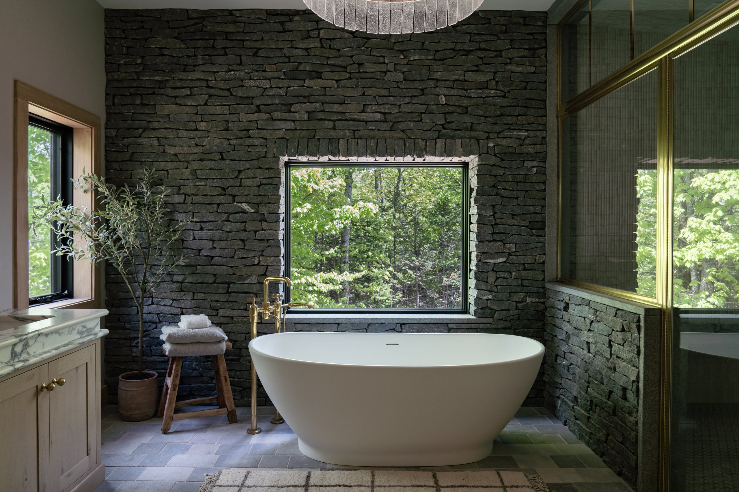 Freestanding tub against a stacked stone wall, finish work by Winter Construction